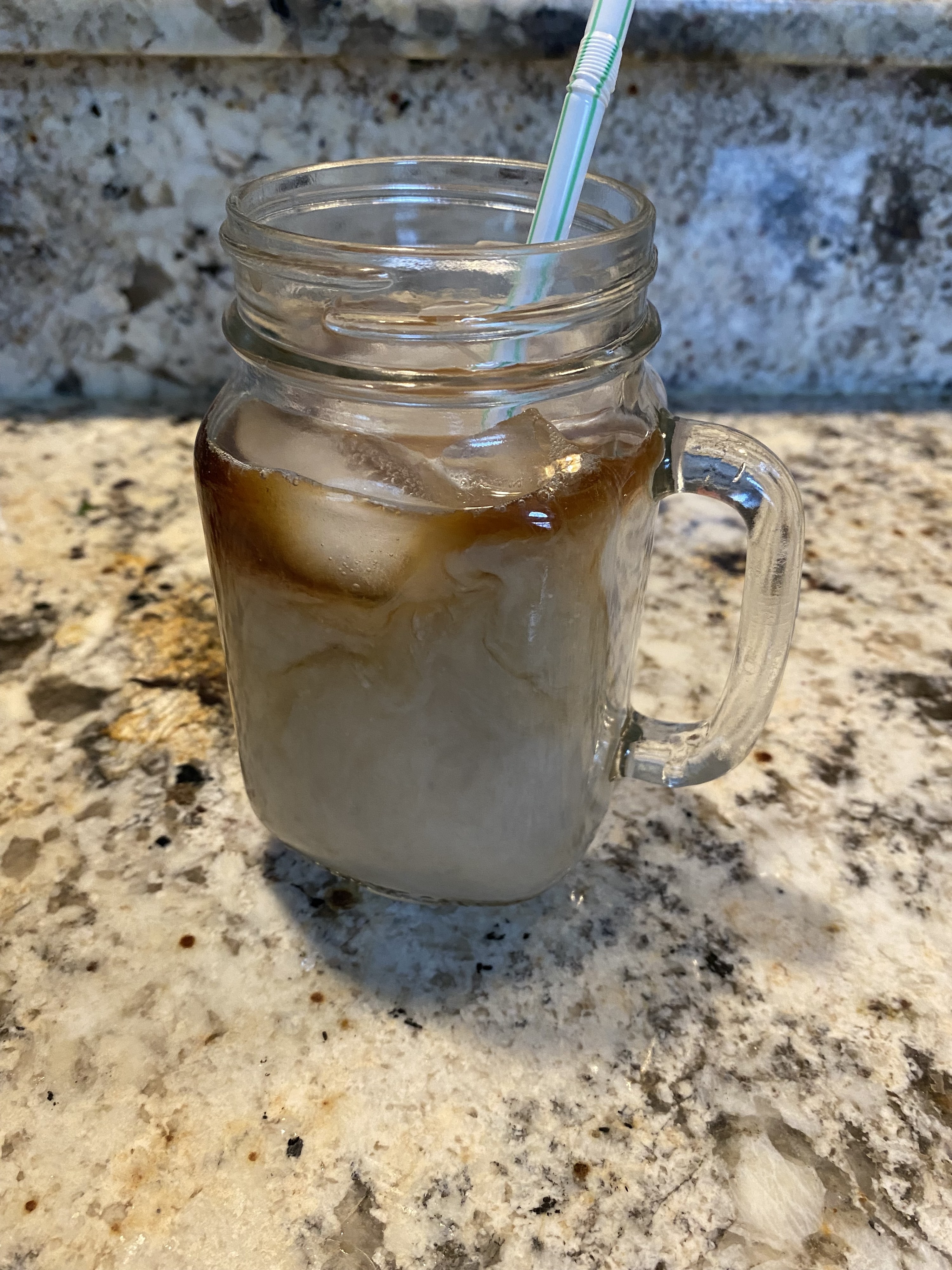 A lightly colored iced coffee drink in a mason jar glass on a counter