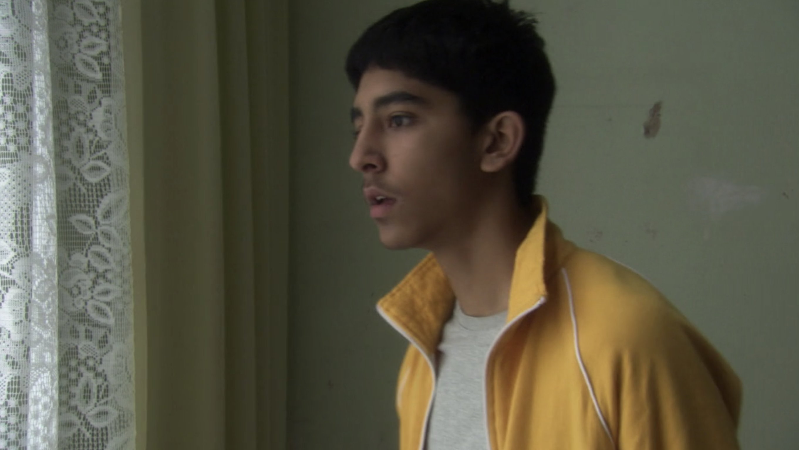 Teen boy in yellow track jacket looking out of window