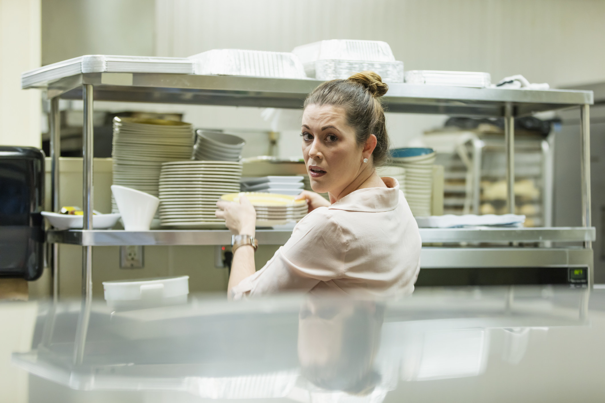 A server looking stressed out in a kitchen while grabbing plates