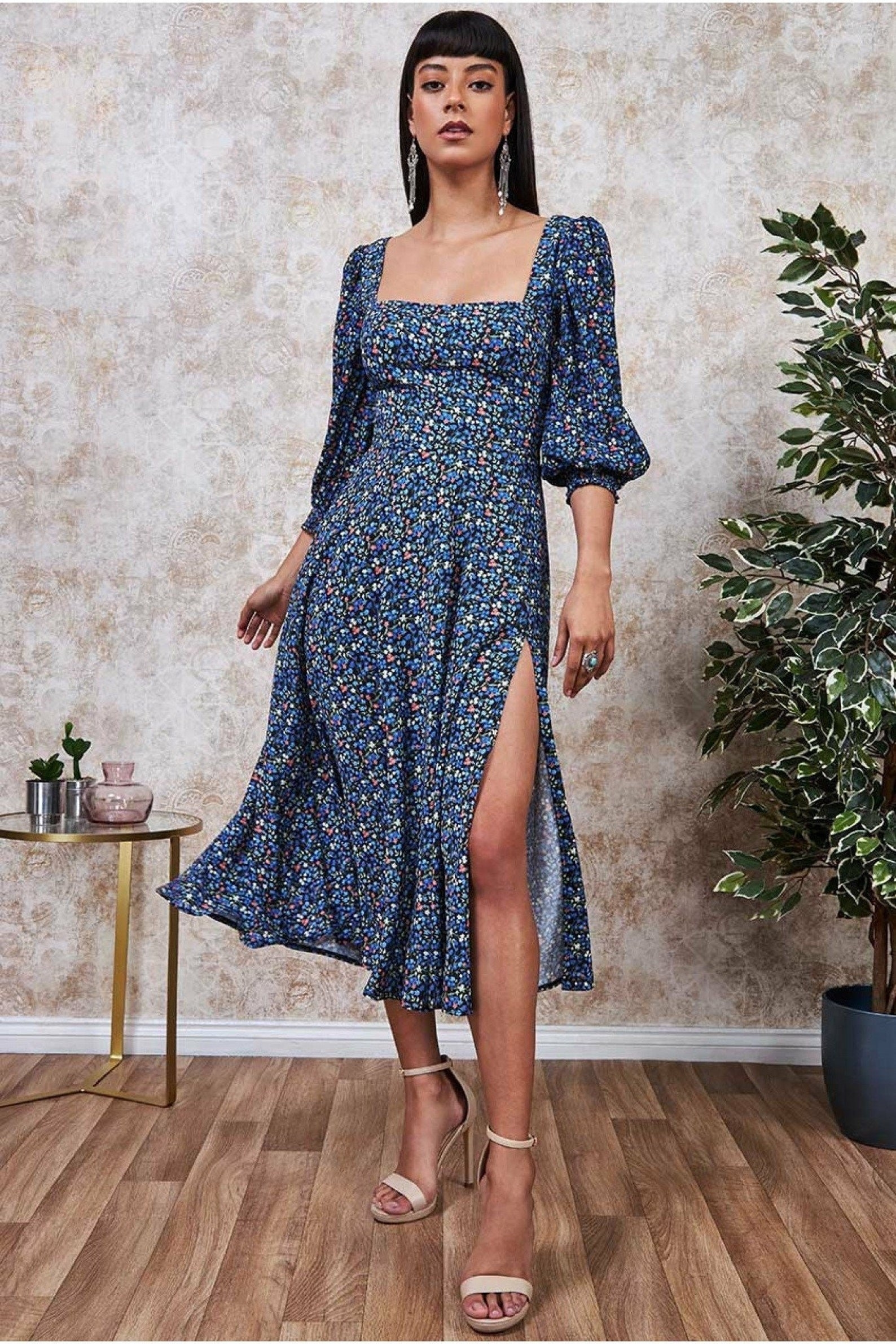 a model wearing the blue floral dress showing the puff sleeves and high slit.