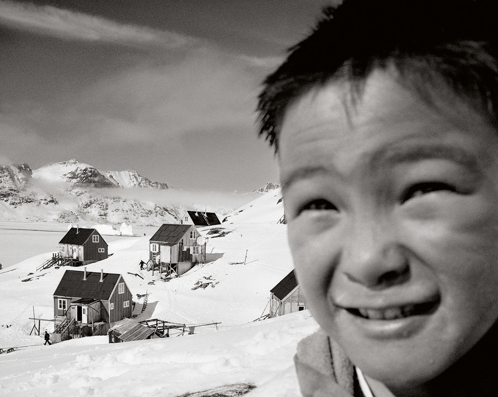 A child smiles into the camera with several small houses amid snow in the background