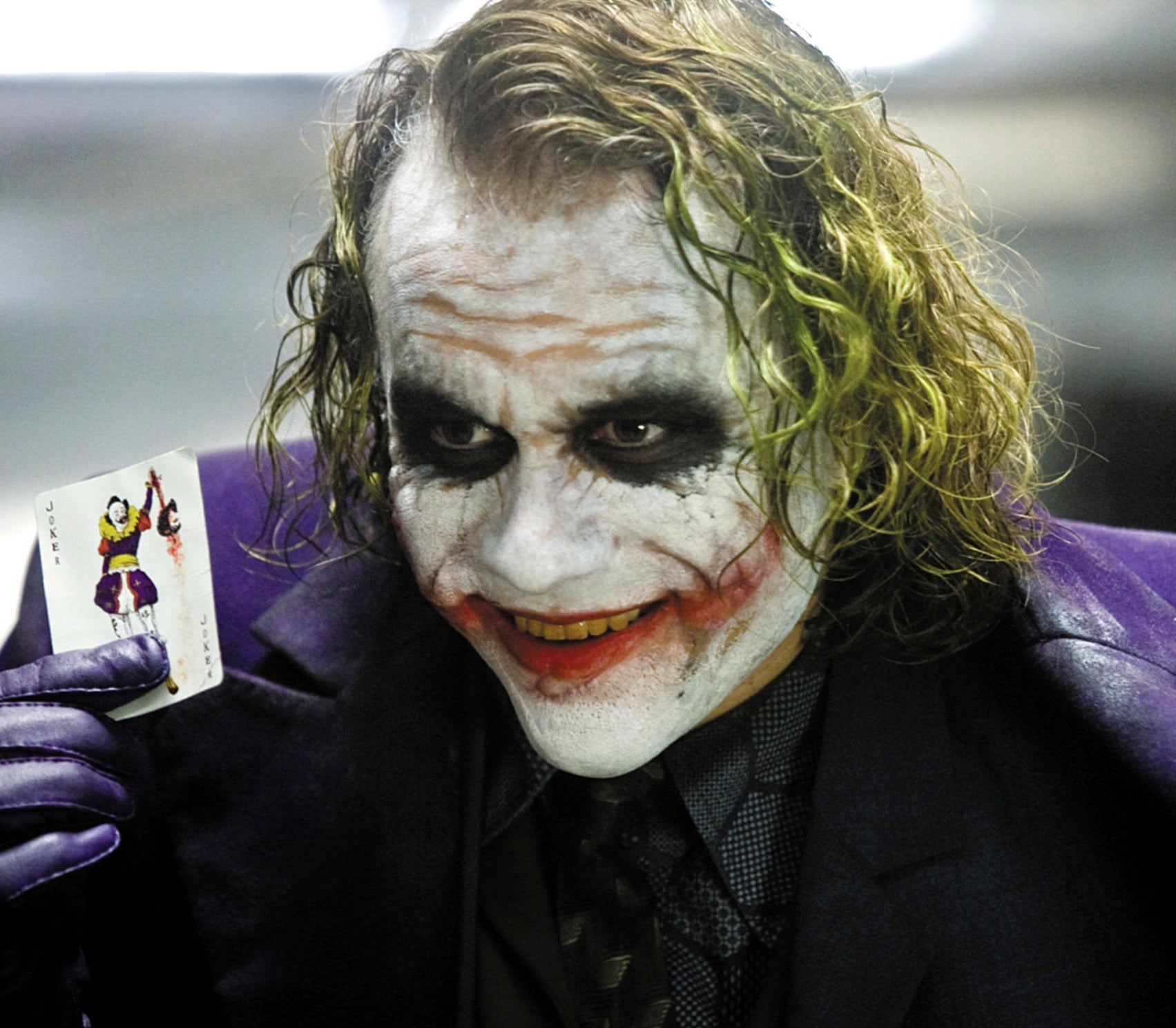 The Joker with smeared makeup holding up a playing card of a joker