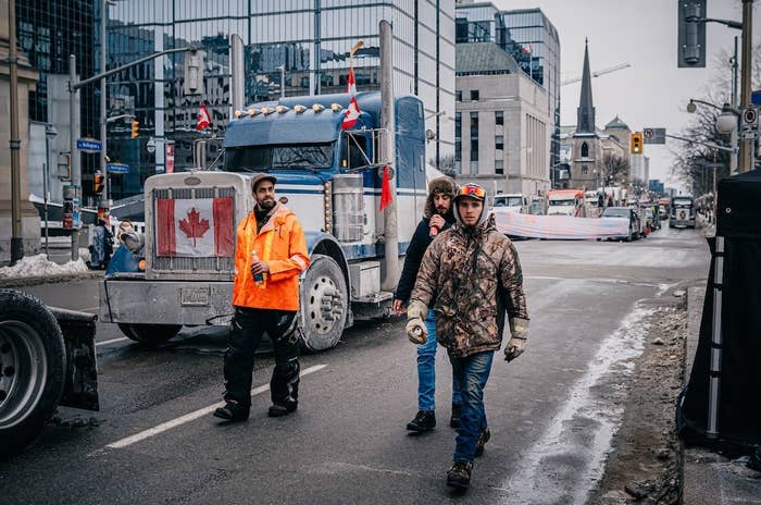 Three people walk alongside a truck with a Canadian flag in front of it