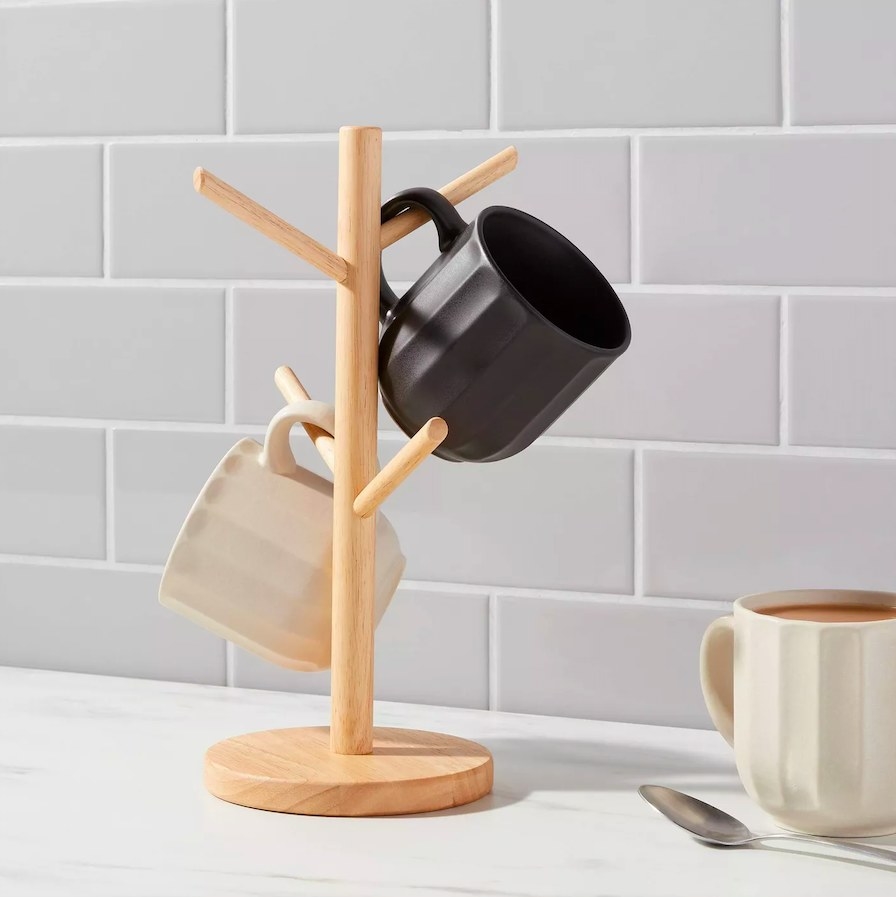 Mug tree with two mugs hanging on it and a mug with a spoon next to it