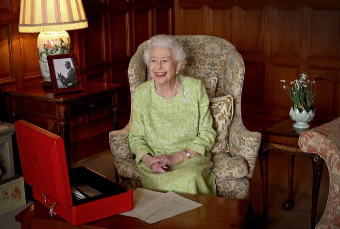 Queen Elizabeth sitting in a high-back chair and smiling with her hands in her lap
