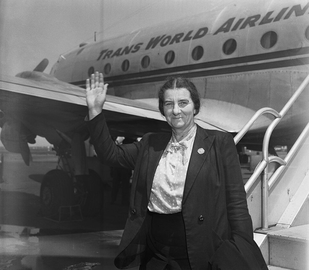 Golda standing in front of a TWA plane and waving