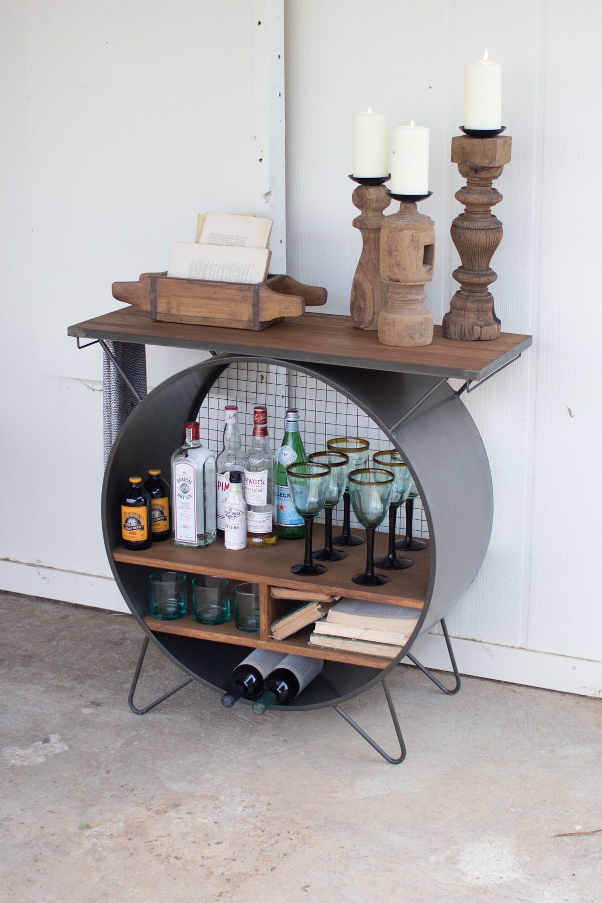 A metal circle with shelves stocked with alcohol, with a piece of wood strapped to the top for an additional shelf.