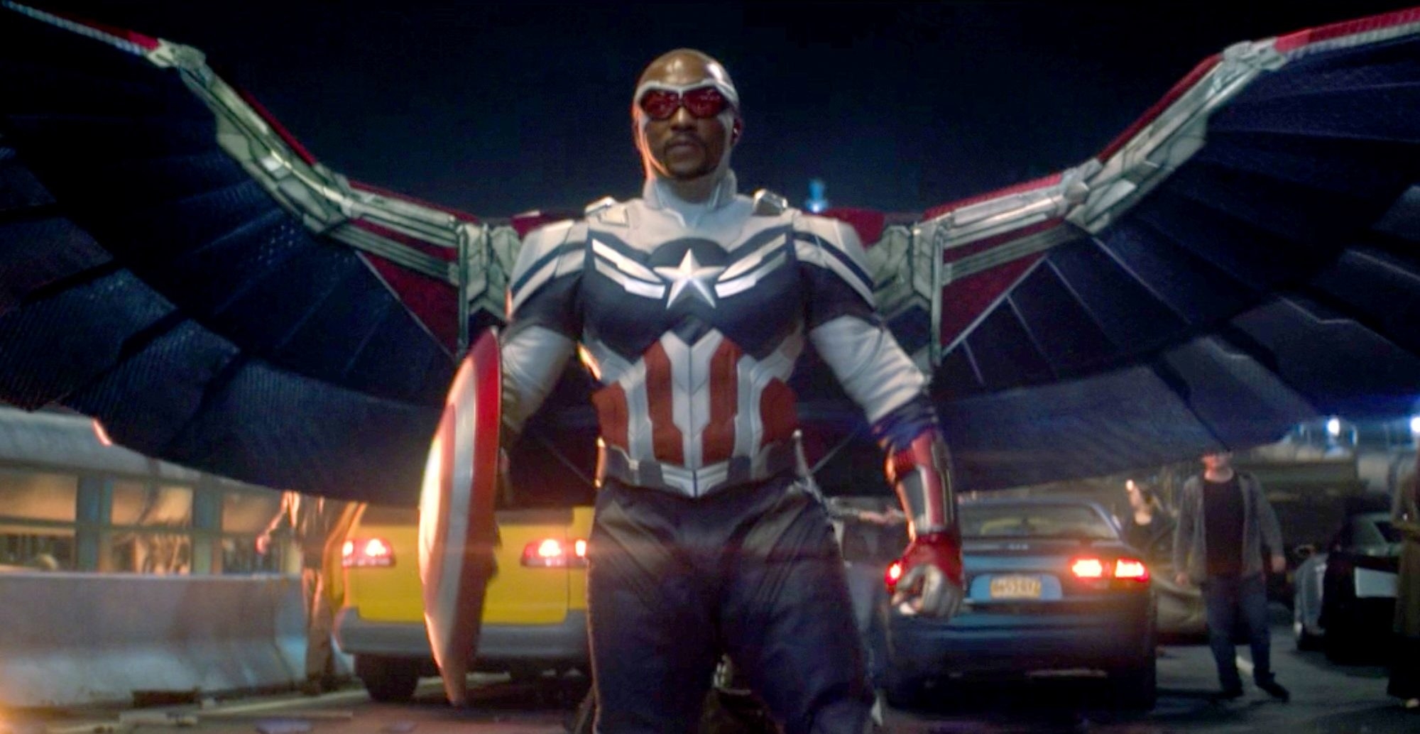 Sam Wilson standing in a road with cars behind him, wearing his winged Captain America outfit and holding the shield