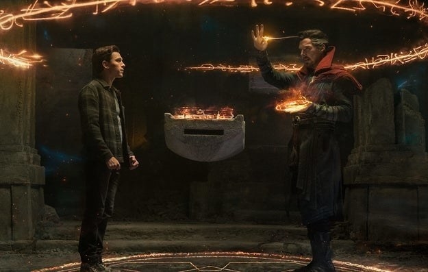 Peter Parker stands in a stone chamber opposite to Doctor Strange, who is casting a spell that creates an orange ring of light filled with symbols around them