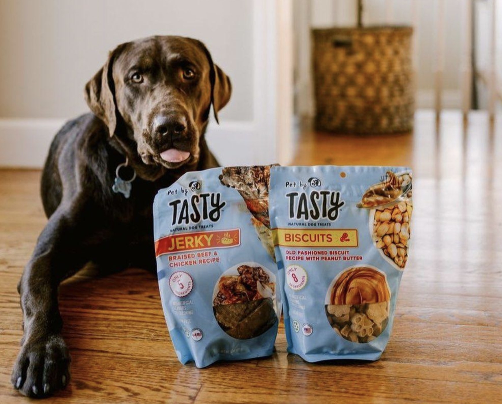 A chocolate lab sitting next to a bag of the jerky treats and peanut butter biscuits