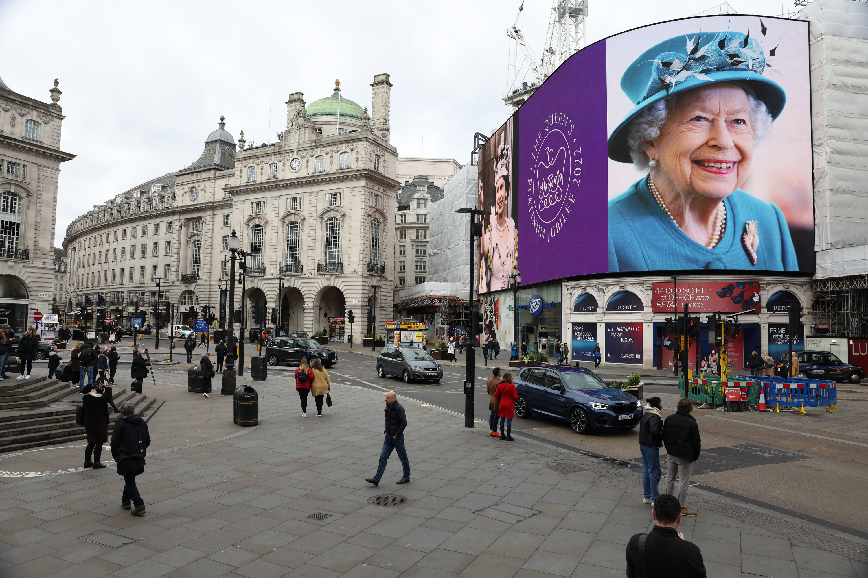 Queen Elizabeth II on a giant screen in London as people walk around on the street 