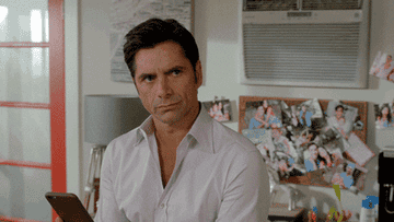 John Stamos looking away and then at his phone typing