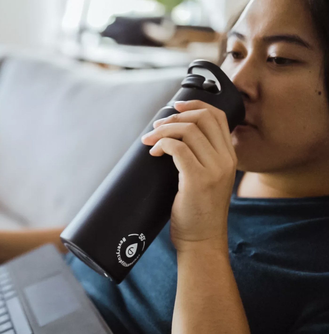 A model drinking from the black flask with her computer in her lap