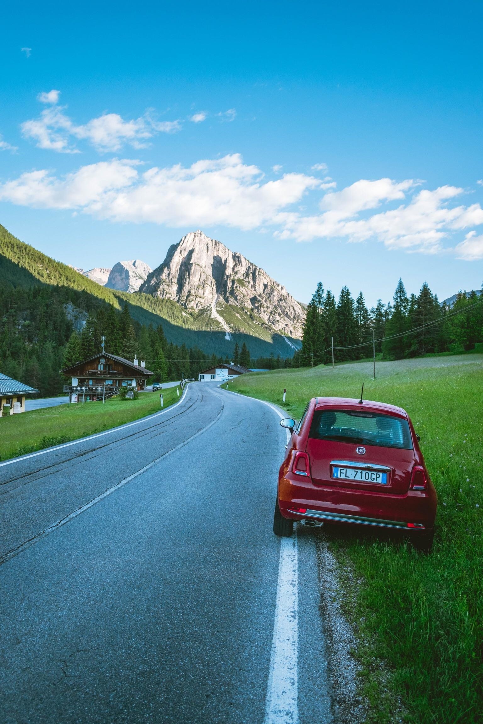 The Dolomite Mountains at the end of a winding road with a red Fiat 500 parked on the side