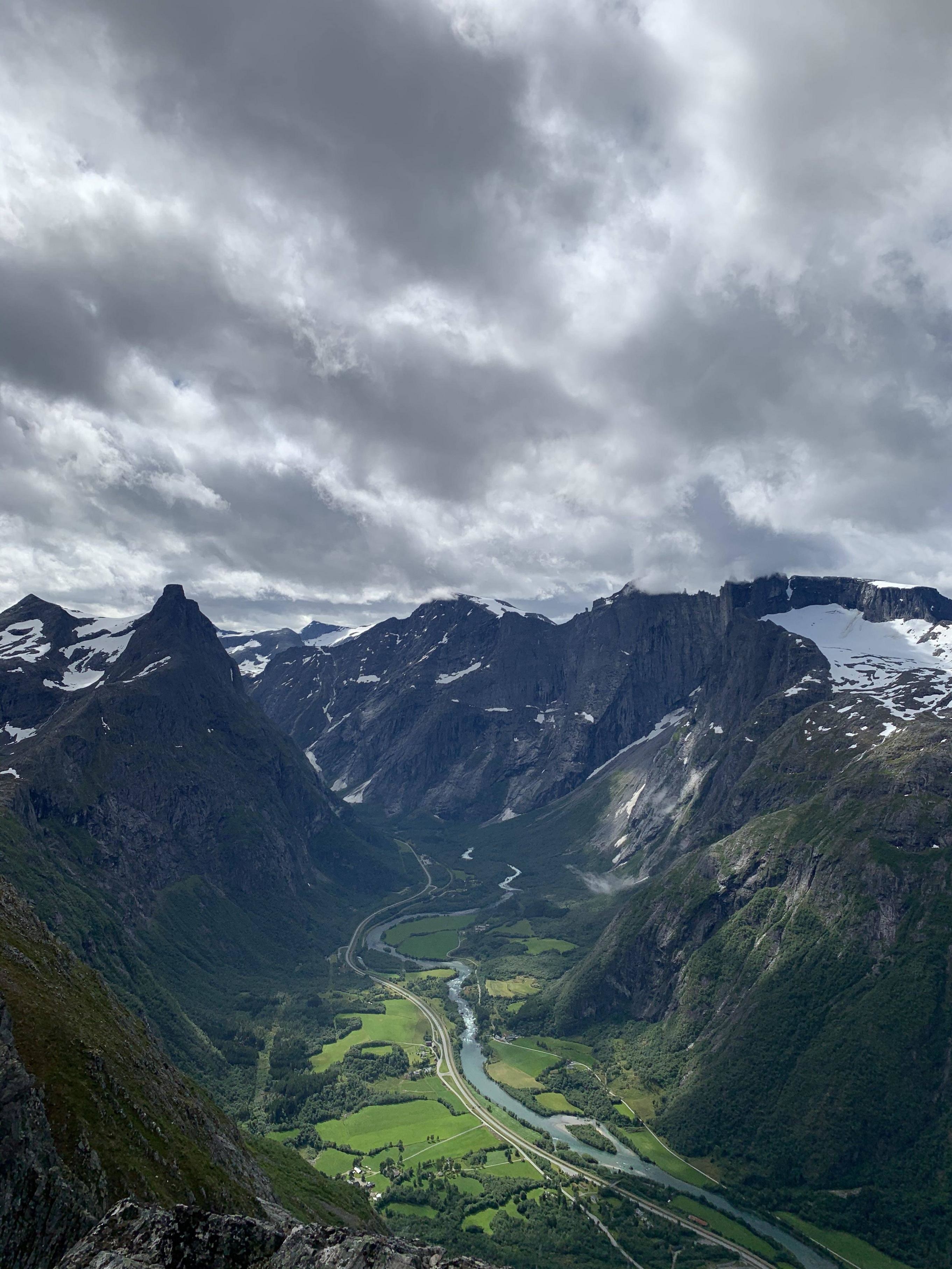 A picture from the top of the mountains in Romsdalen, with a river and lush green field below in the valleys