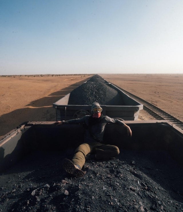 A person sitting in a train cart, on top of a pile of iron ore, in the Sahara