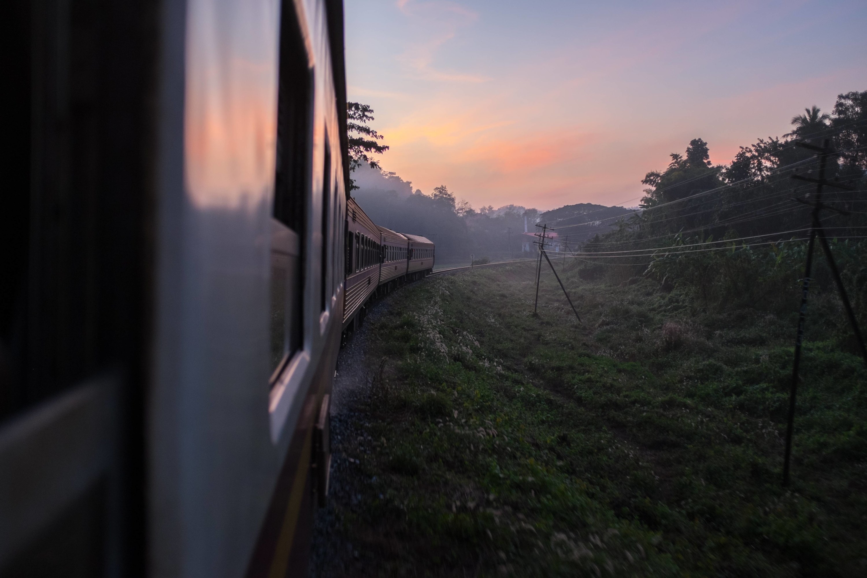 the end of a train, taken from a window within, as the train travels through lush greenery to Chiang Mai from Bangkok