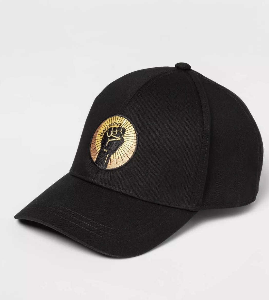The black cotton hat has a gold circular logo with a black fist and &quot;STAY STRONG&quot; written above
