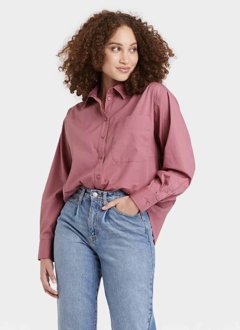 An adult is wearing a rosey purple oversized button-up shirt tucked into jeans
