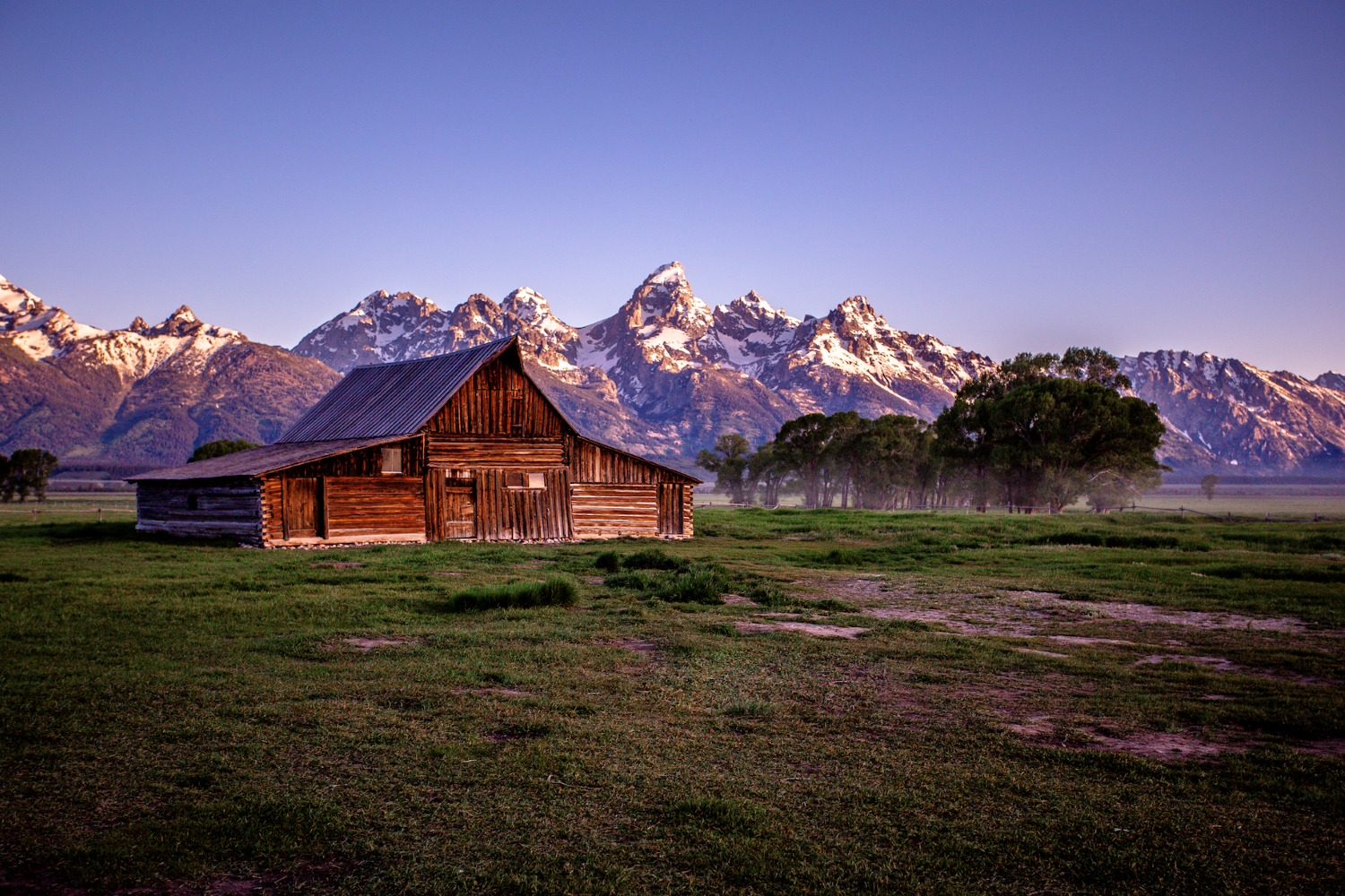 a log cabin sitting in front of purple-looking mountains in Grand Teton National Park