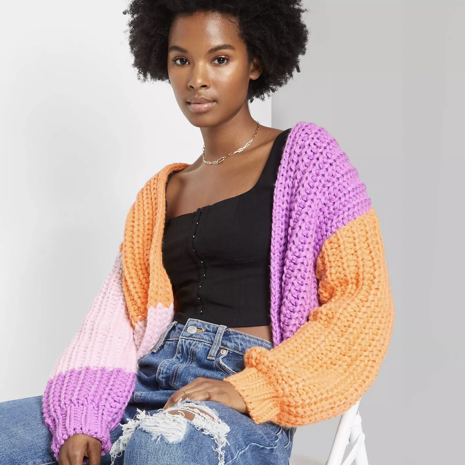 An adult is wearing a thick cableknit sweater with orange, pink and piurple chunks of color