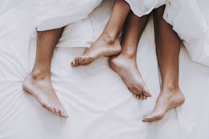 A couple&#x27;s feet peak out of bed covers