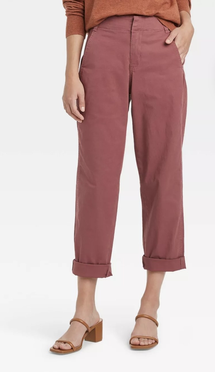 An adult is wearing burgundy chino pants cuffed at the ankle and brown strappy sandal heels