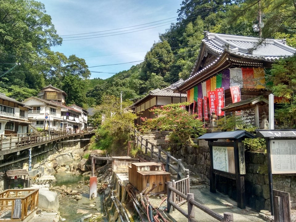 a bath houe with colorful flags sitting alonside a river in Kumano