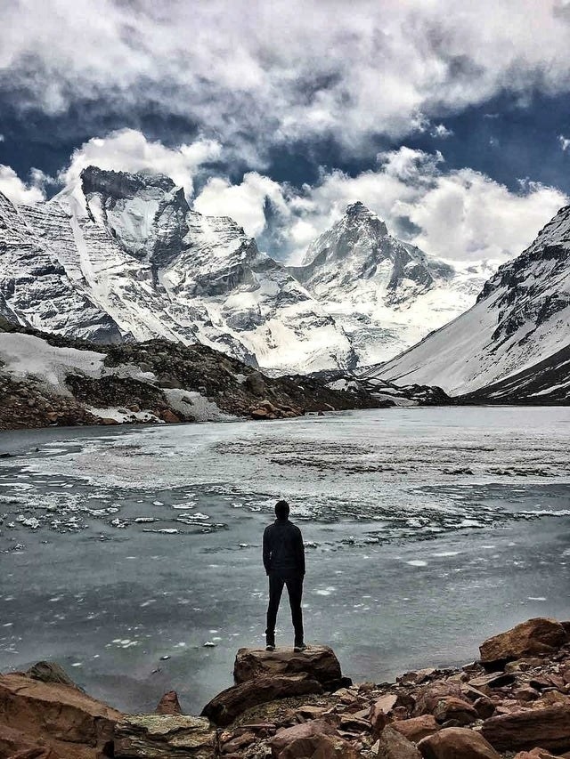 a person stands on a rock overlooking Kedartal Lake, in the Garhwal region of the Himalayas in India