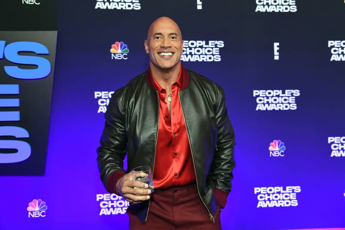 The Rock holds a glass while posing at a step-and-repeat at the People&#x27;s Choice Awards
