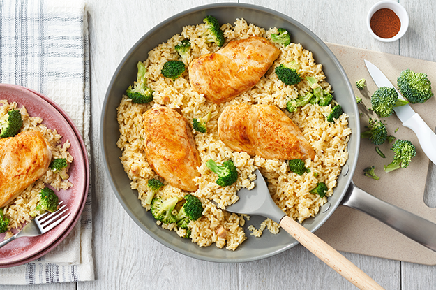 Chicken and rice in a pan beside broccoli on a cutting board