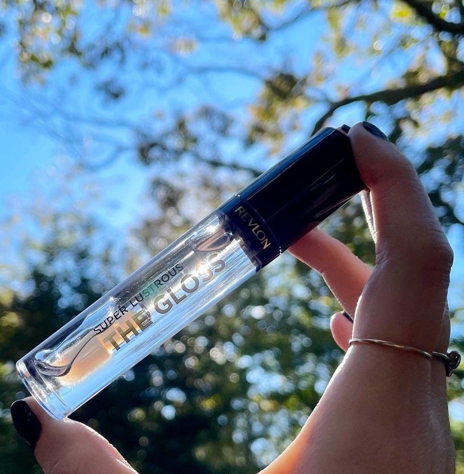 A person holding the tube of gloss between their thumb and finger