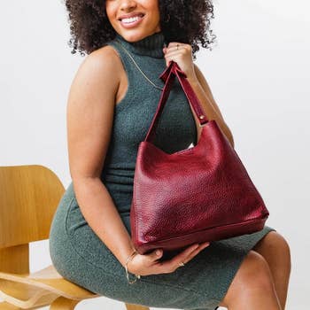 model sitting down with the bag on their lap. it has no outside pockets, a long strap, and an open top.