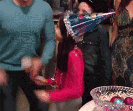 a gif of a little girl wearing a birthday hat and yelling yeah while throwing stuff on the floor
