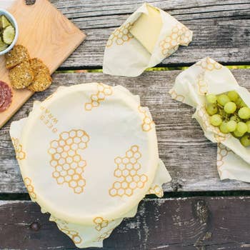 the honeycomb pattern wrap used to cover a bowl of food, a block of cheese, and a bundle of grapes