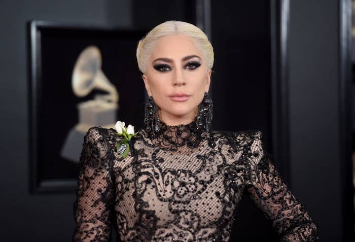 Lady Gaga posing on the Grammys red carpet in a lace gown with a small flower attached to her shoulder