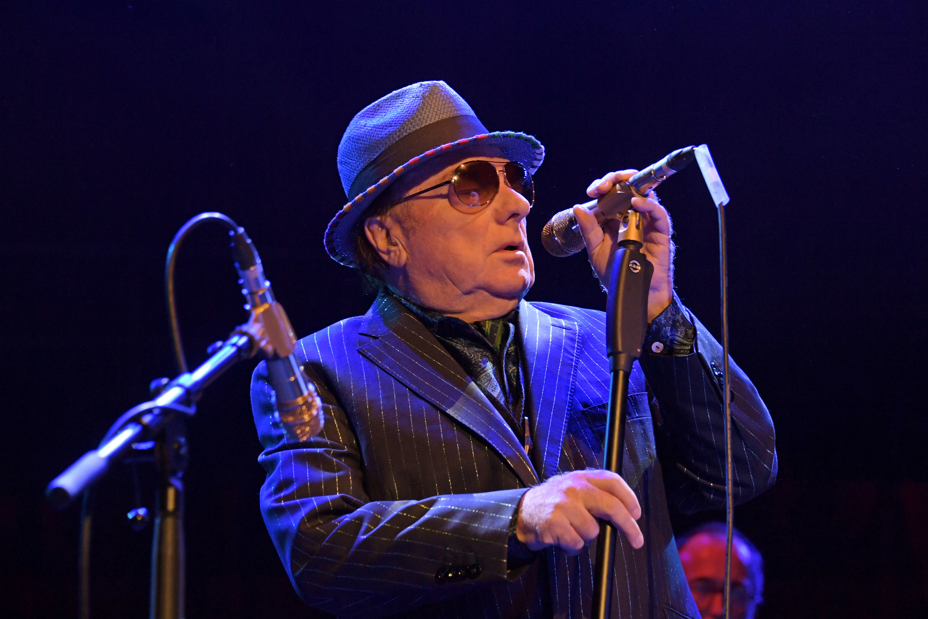 Van Morrison holding a mic stand as he performs onstage