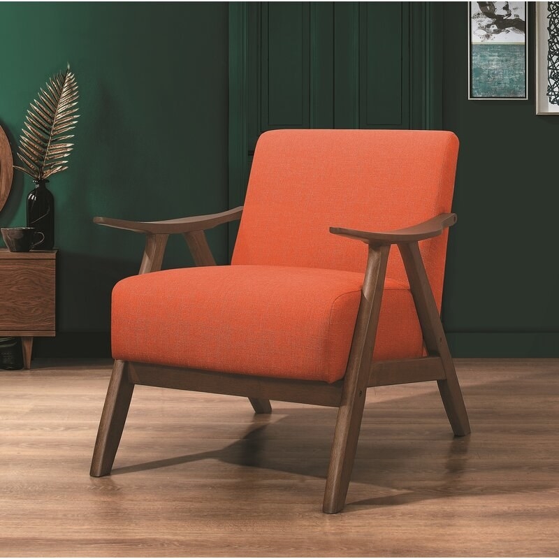 A mid-century modern looking chair with orange cushions in a dark green living room.