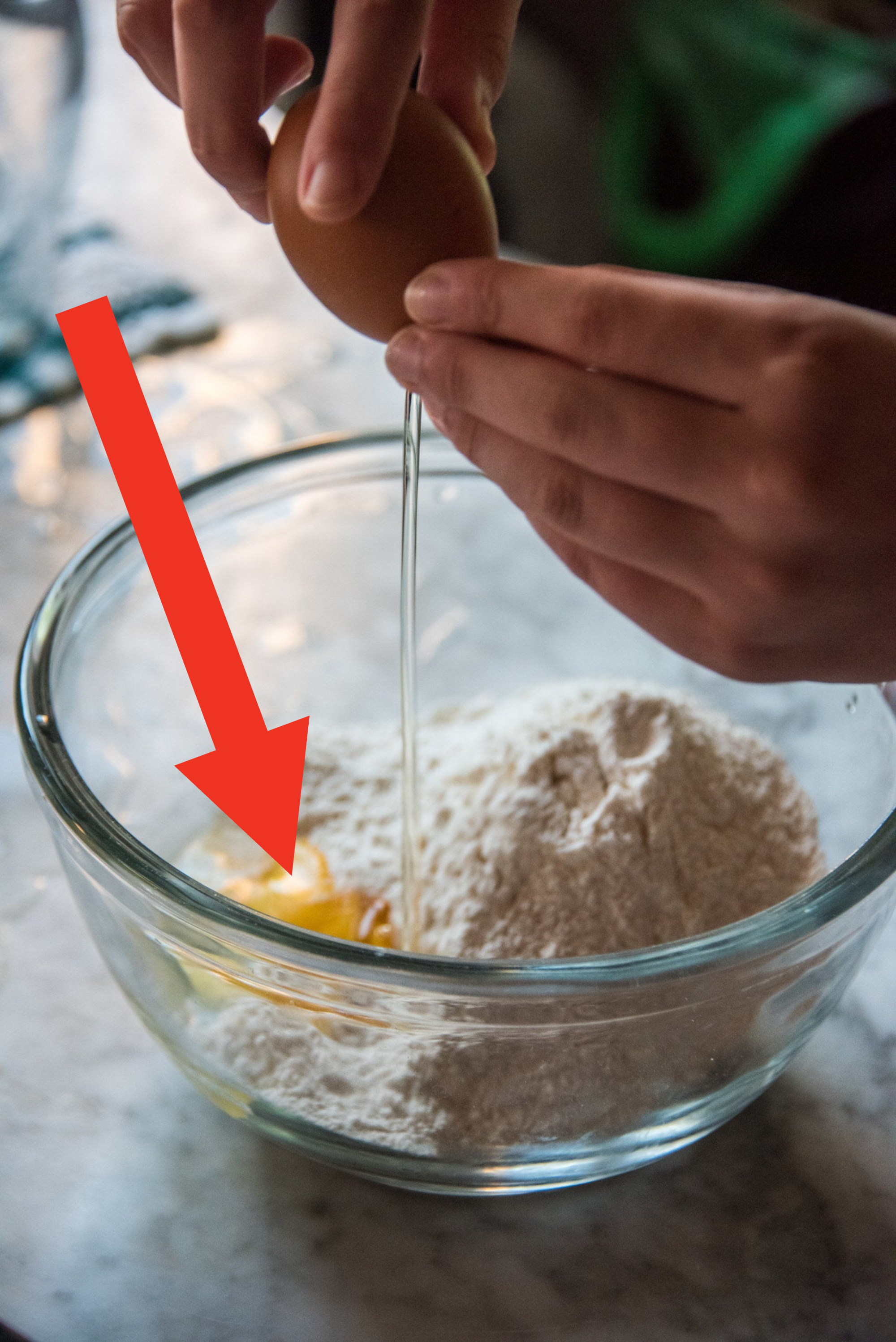 Cracking an egg into a bowl with white flour.