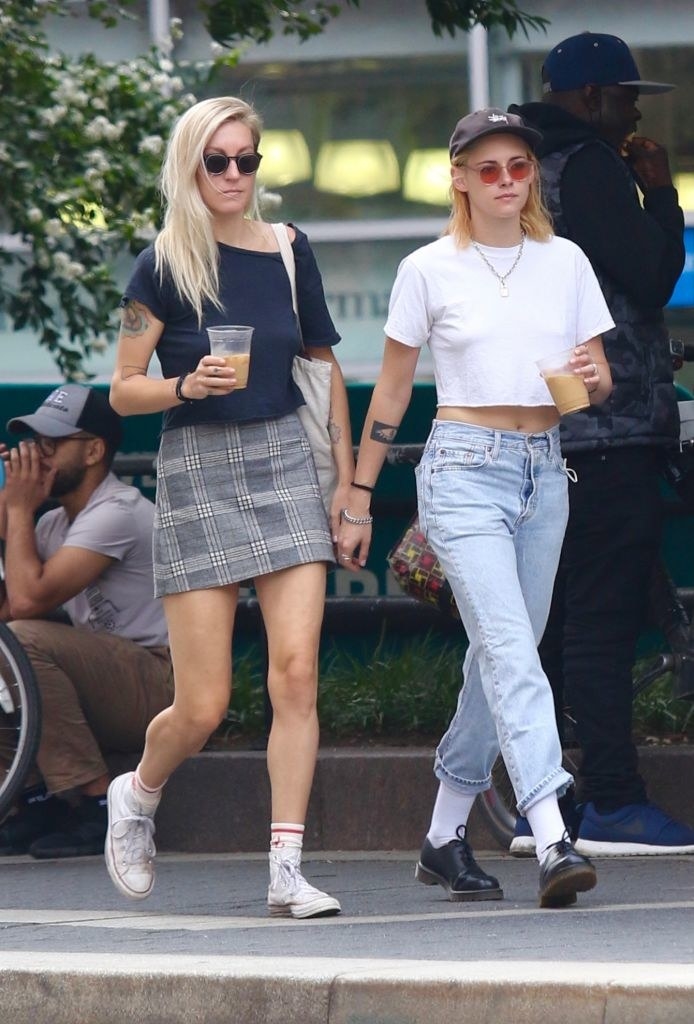 The couple walking down a sidewalk hand-in-hand while holding iced coffees