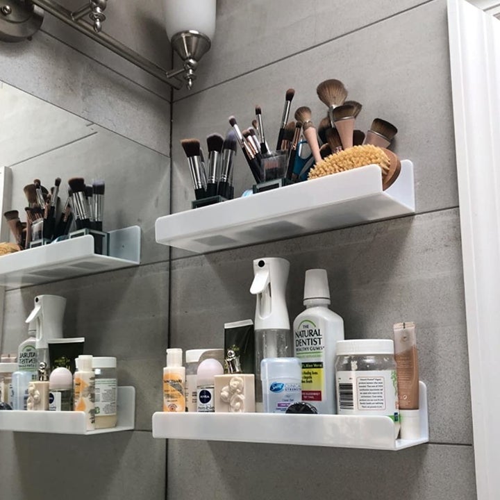 a reviewer photo of two shelves installed by a bathroom vanity and filled with various makeup and skincare products