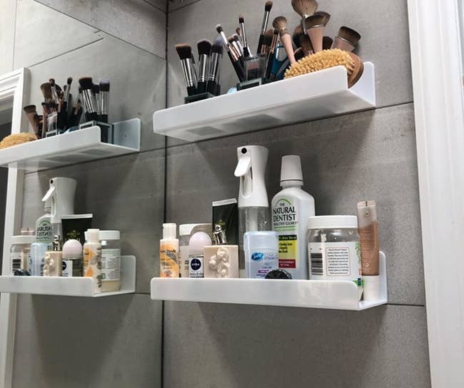 a reviewer photo of two white shelves installed by a bathroom vanity and filled with various makeup and skincare products