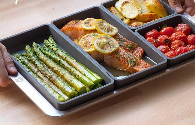 the four pan dividers with vegetables and salmon and carbs being cooked separately