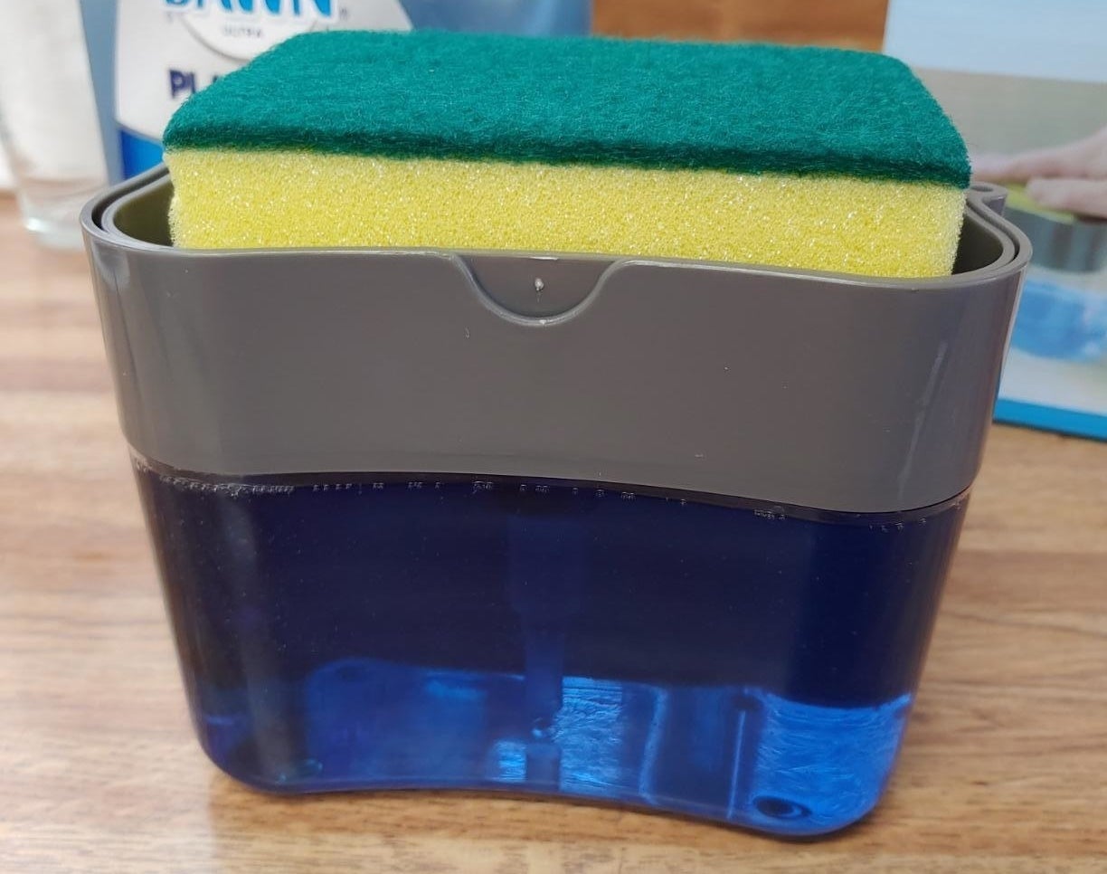 A sponge resting in the dispenser caddy that's filled with dish soap