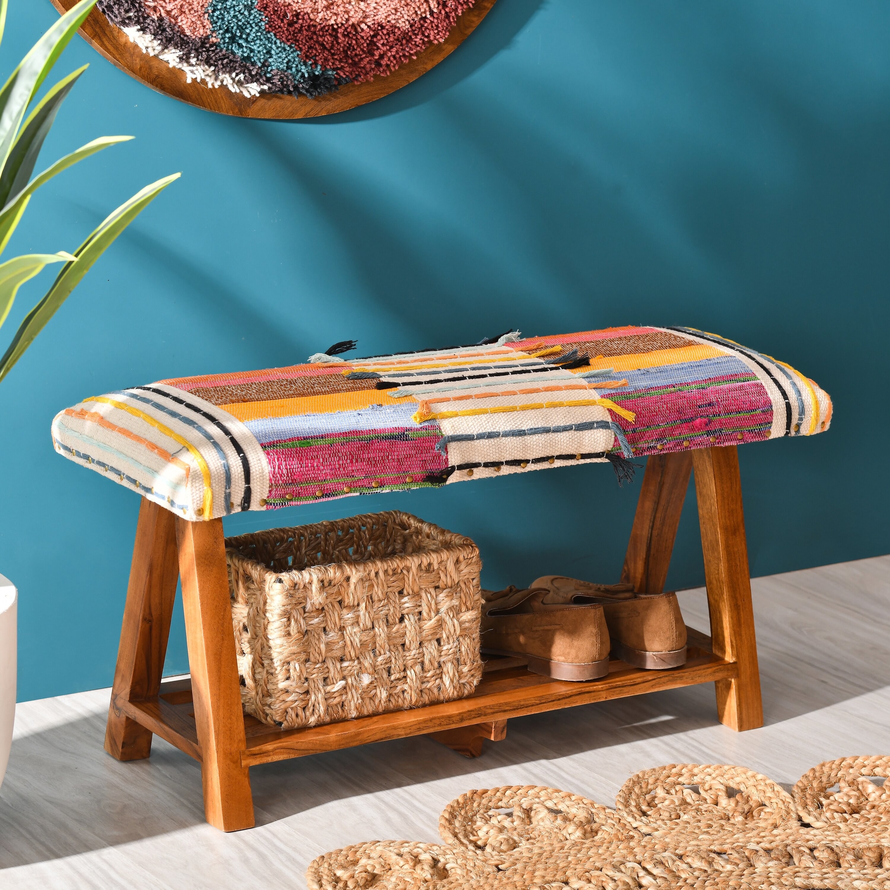 a multicolored upholstered storage bench with wood shelf beneath holding a basket and shoes