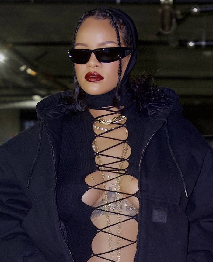 A closeup of Rihanna wearing a black jacket and top with criss cross string in the opening in the middle