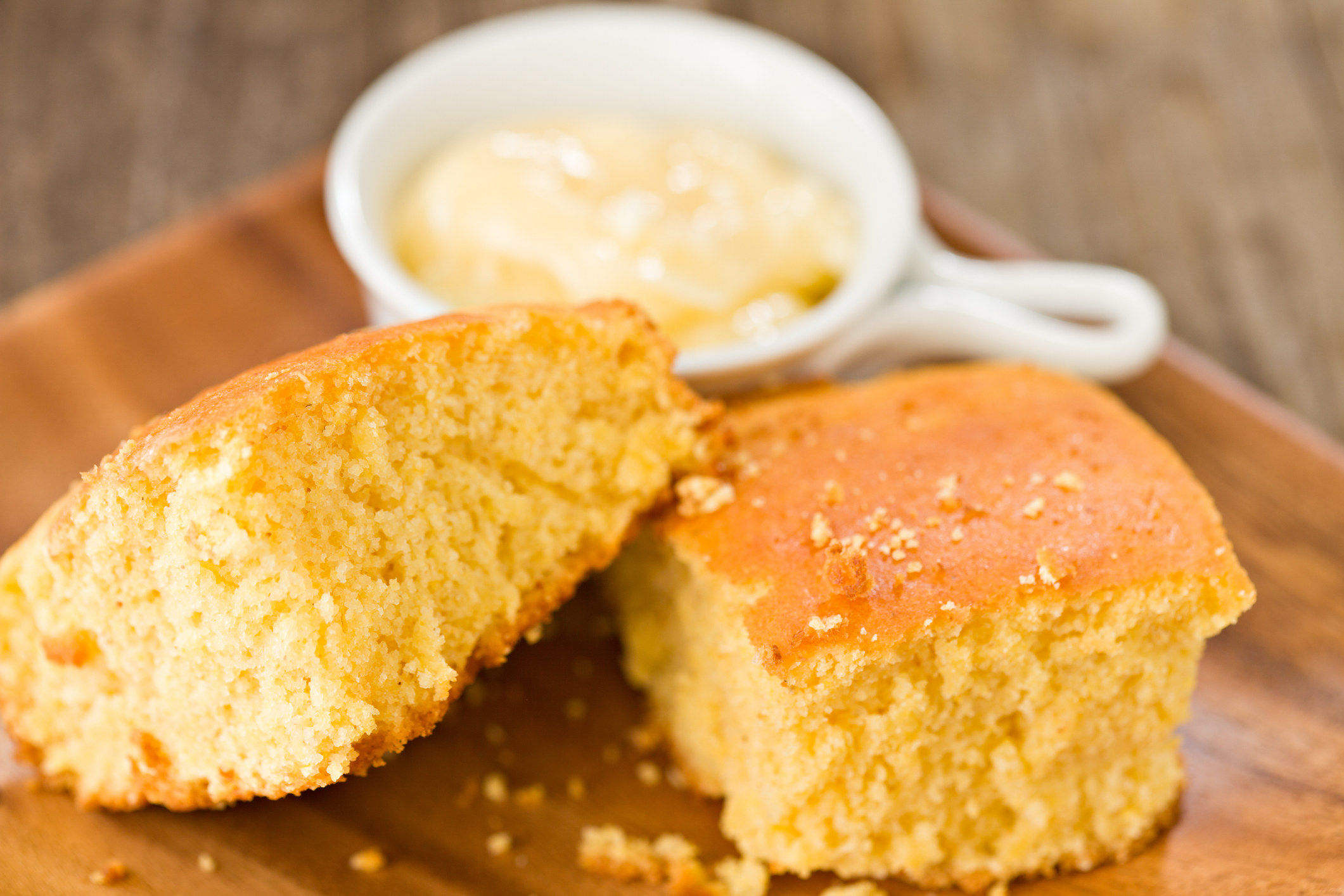 Two freshly baked slices of cornbread and a container with honey butter