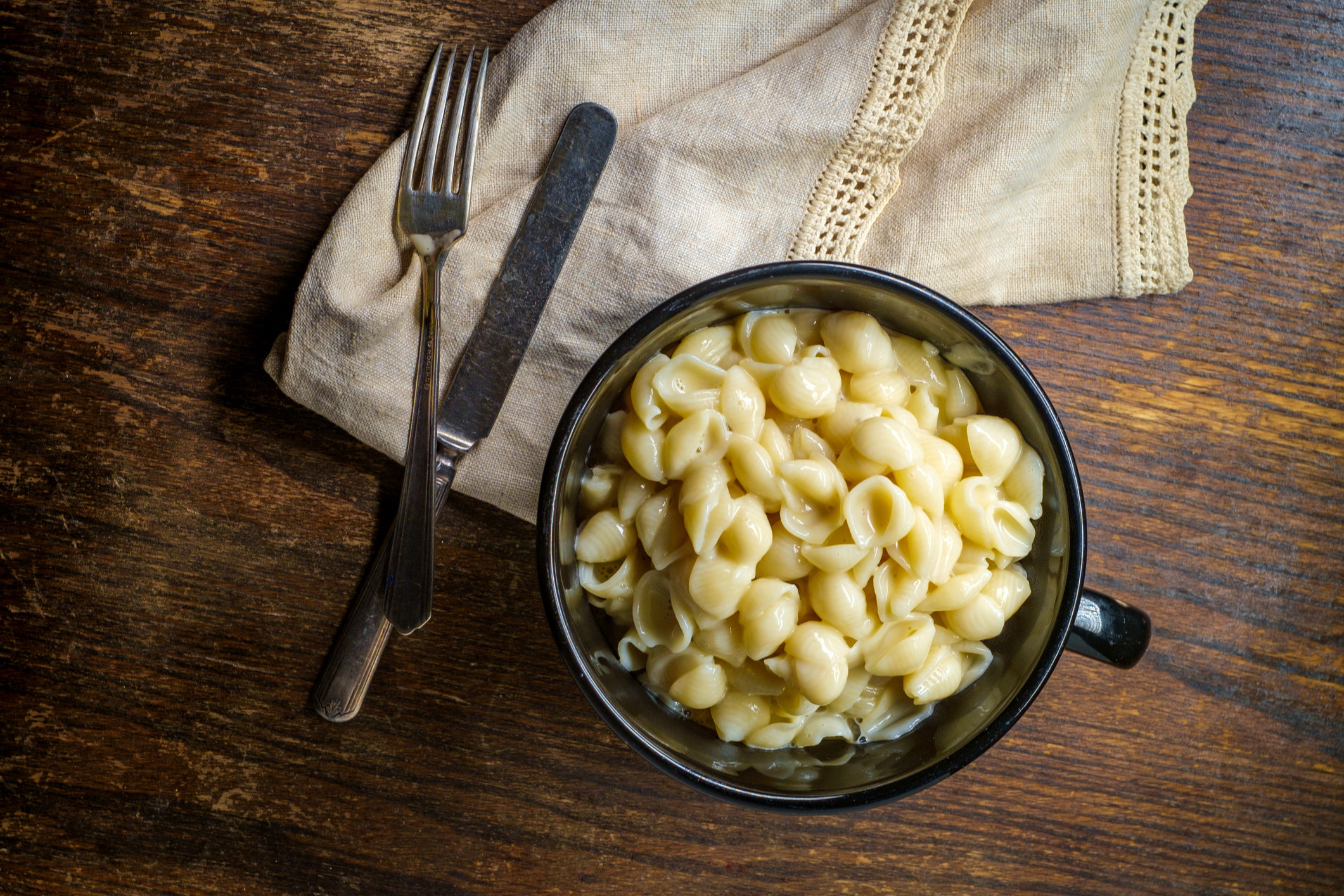 Bowl of pasta and cheese on a wooden table with a fork and napkin beside it