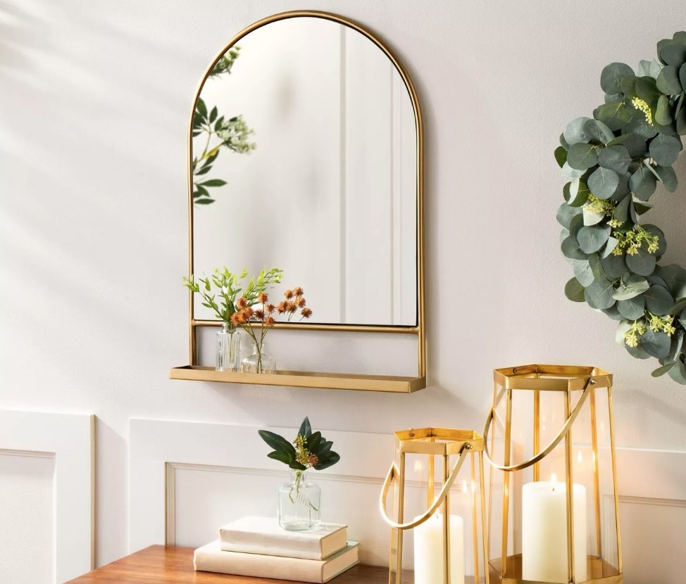 An arched gold metal framed mirror with an attached shelf
