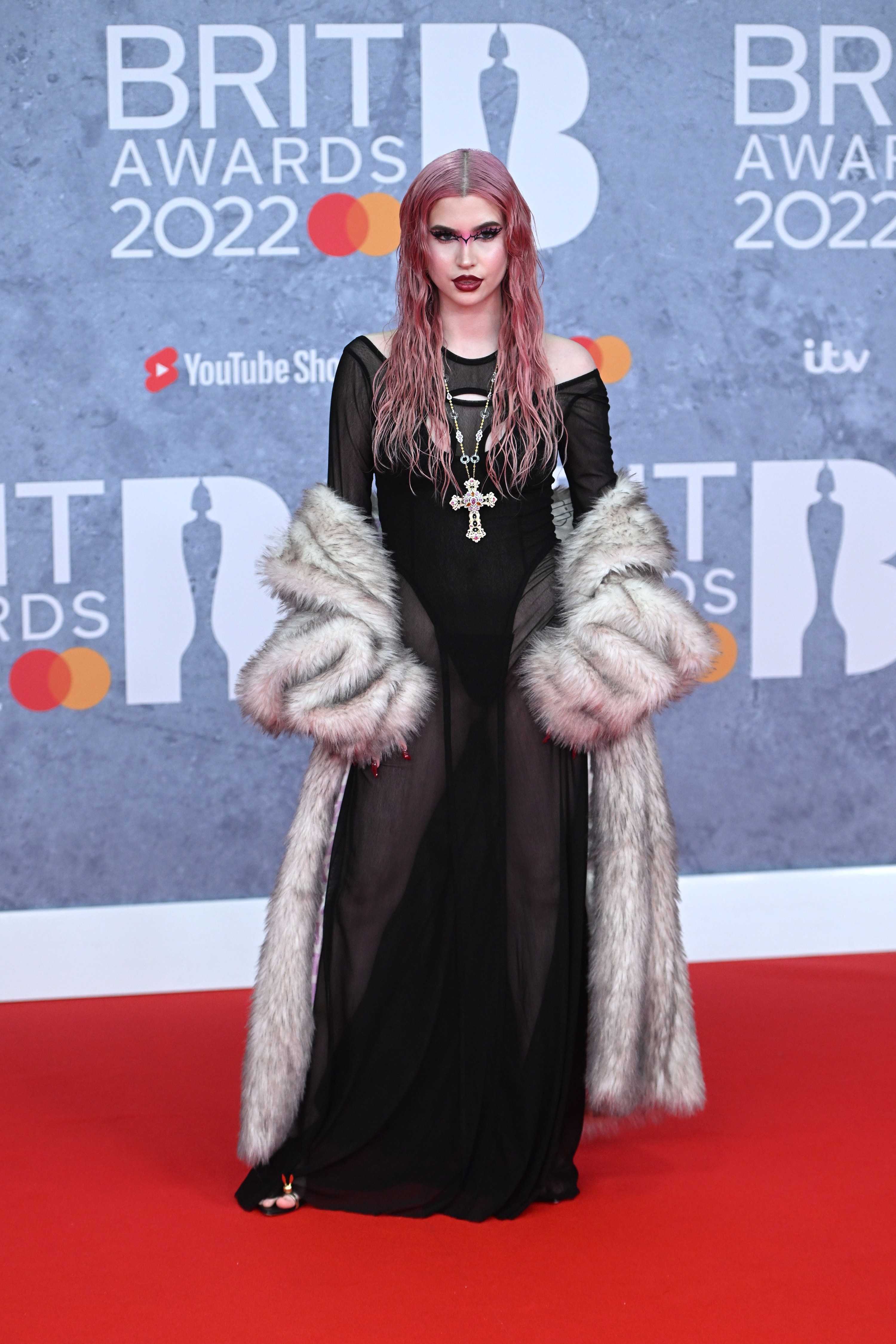 Abby wears a long sheer dress with a black bodysuit and a fur coat